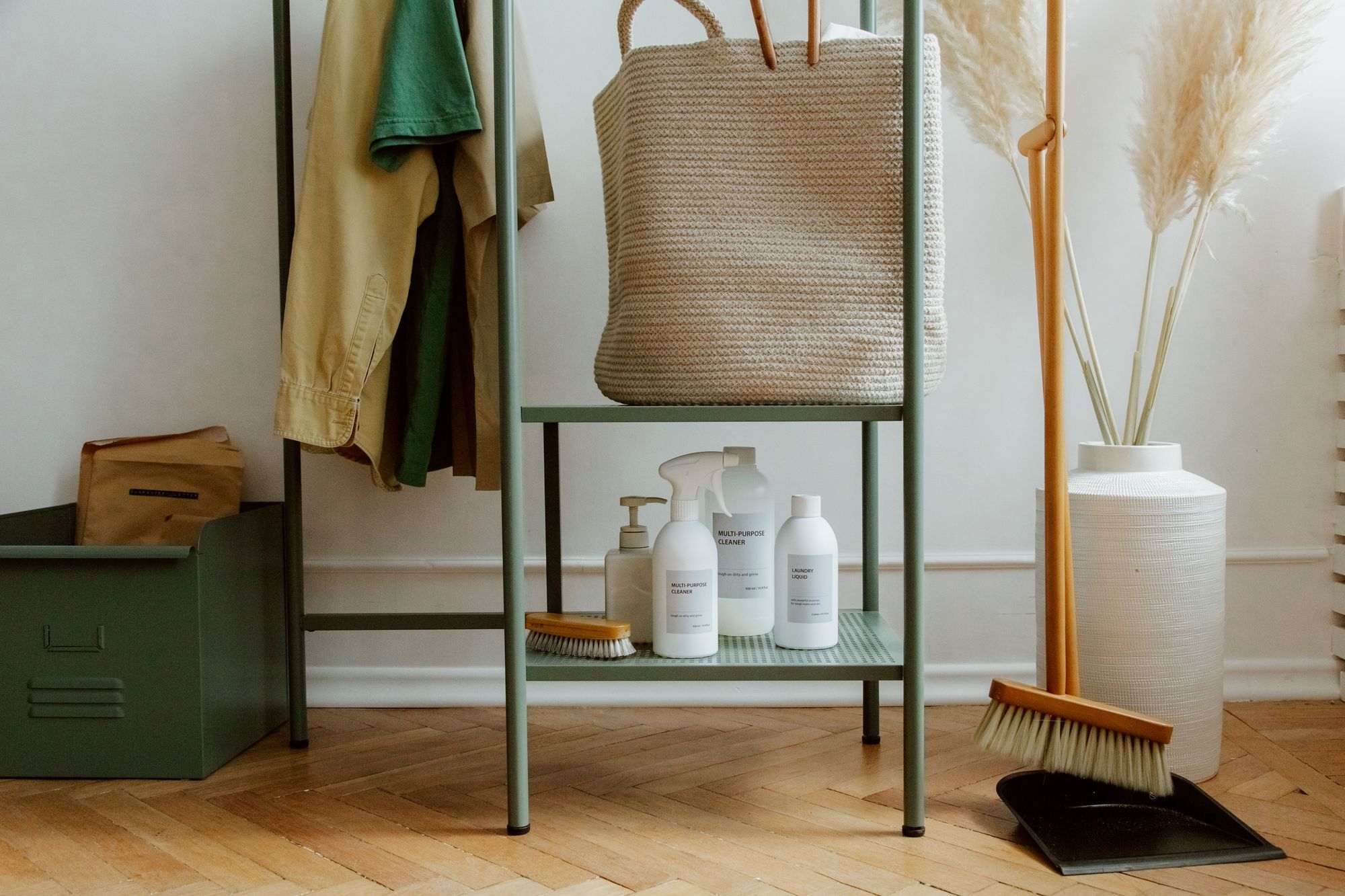 Escoba, recogedor y botellas de limpieza junto a un mueble verde en la entrada de una casa
